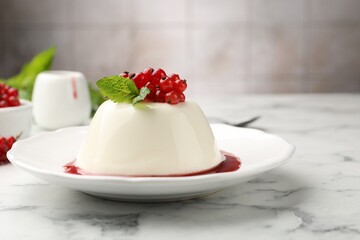 Delicious panna cotta with red currants, sauce and mint on white marble table against blurred background, closeup