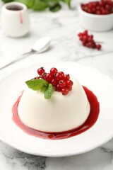 Delicious panna cotta with red currants, sauce and mint on white marble table, closeup