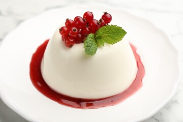 Delicious panna cotta with red currants, sauce and mint on white marble table, closeup