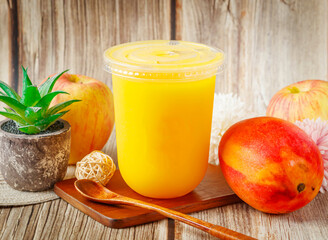 Fresh Mango Apple Juice in Plastic Cup with Spoon, Apples, and Mango on Rustic Wooden Background