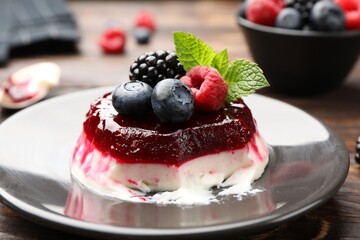 Delicious panna cotta with berries, jam and mint on wooden table, closeup