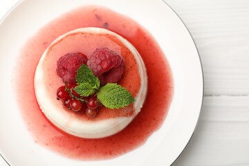 Delicious panna cotta with berries, sauce and mint on white wooden table, top view