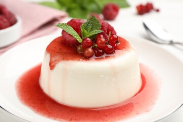 Delicious panna cotta with berries, sauce and mint on white table, closeup