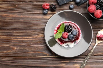 Delicious panna cotta with berries, jam and mint on wooden table, flat lay. Space for text