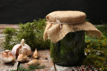 Pickled cucumbers in jar, garlic and dill on color wooden table against black background, closeup