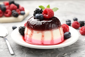 Tasty panna cotta with berries and jam on light grey table, closeup