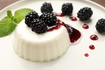 Tasty panna cotta with blackberries, mint and sauce on table, closeup