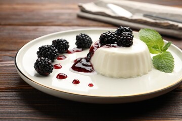 Tasty panna cotta with blackberries, mint and sauce on wooden table, closeup