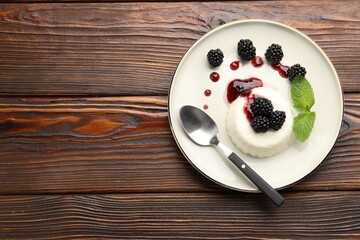 Tasty panna cotta with blackberries, mint and sauce on wooden table, top view. Space for text