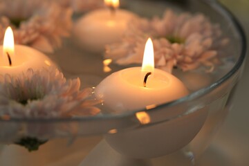 Burning candles and flowers in bowl of water on table, closeup