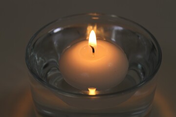 Burning candle in glass of water on table, closeup