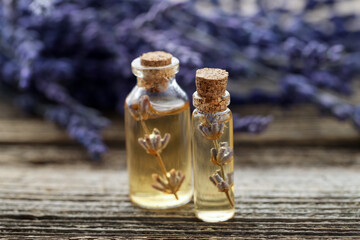 Lavender essential oil in bottles with flowers on wooden table, closeup
