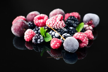 Many different frozen berries and mint on black table, closeup