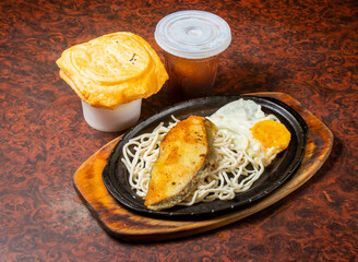 Golden Fish Fillet with Noodles and Fried Egg on a Hot Plate side view of hong kong food