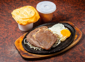 Sirloin Steak with Noodles and Fried Egg on a Hot Plate side view of hong kong food