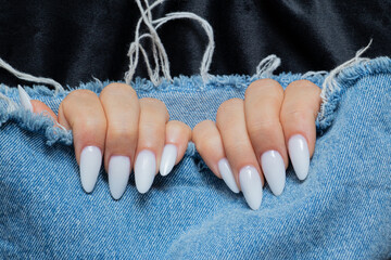 Female hands with long sharp white manicure on ripped jeans on black background