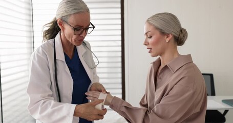Female doctor wrapping woman patient wrist with white bandage, treating physical injury during medical visit. Clinical first aid or orthopedic care, sprain, strain, tendonitis, minor fracture injury - Powered by Adobe