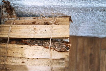 Bundle of dry birch firewood tied with hemp rope lies near a whitewashed stove wall, rustic countryside heating concept