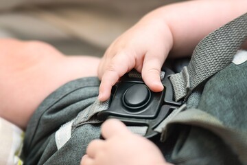 Fototapeta premium Child's hands trying to open a plastic buckle on car seat safety straps, kids learning independence concept