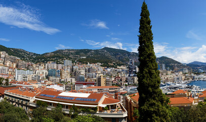 Obraz premium Elevated view of a Monaco cityscape with layered high-rises and red rooftops nestled in green hills.
