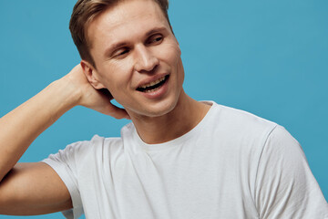 Smiling man with short brown hair in casual white t-shirt, looking to the side, holding hand behind neck, cheerful expression, blue background, studio portrait, positive mood, lifestyle concept