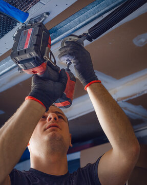 Low angle view of a worker fastening a spring on a garage door mechanism during installation or repair.