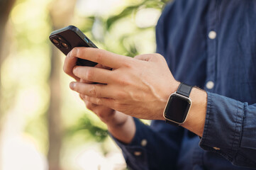 In a beautiful natural setting, a young man is using his smartphone and wearing a stylish smartwatch