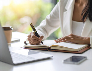 A businesswoman holds a pen while writing notes in a notebook at her desk