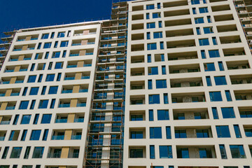 Fototapeta premium New residential buildings near completion with scaffolding and blue sky on a sunny day in a bustling urban area