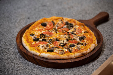Close-up of fungi pizza with fresh mushrooms, black olives, sliced tomatoes, and mozzarella on tomato sauce, served on a marble counter for a gourmet Italian dining experience.

