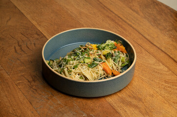 Classic Aglio e Olio pasta with spaghetti, garlic, olive oil, chili flakes, olives, parmesan, parsley, and cherry tomatoes, served in a blue ceramic plate on a brown table.

