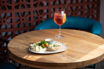 Plated chicken steak with creamy pepper sauce, garlic butter sautéed vegetables, mashed potatoes, and mixed herbs, served on brown table with sunlight and chair in background.










