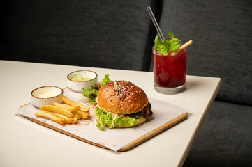 Classic crisp chicken burger with romaine, crumb-fried chicken, chipotle mayo, jalapeños, and fried egg, served with fries, dips, sauce, and a strawberry cocktail on a white table.

