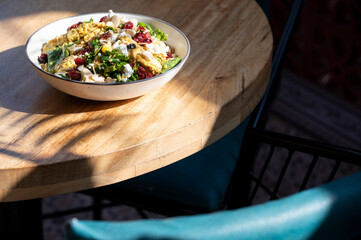 Fresh Green Crunch non-veg salad with kale, grilled mushroom, beans, olives, chicken, feta, cranberry, nuts, and carrot orange vinaigrette on a brown table in warm sunlight.