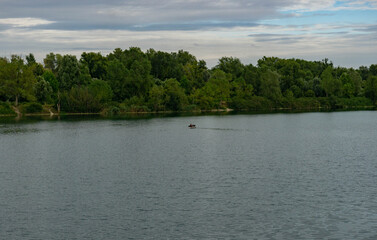 Man Fishing on Boat in Countryside Lake with Forest on the Background