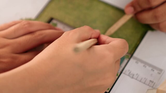 A video of architect using ruler and pencil to measure blueprint scale. Designer designing house construction on a table at studio with architectural plan scattered around. Focus on hand. Delineation.