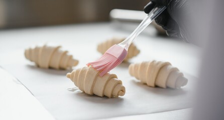 Baker glazing croissants with silicone brush in bakery