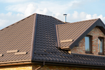 Brown tiled roof of a brick house under bright cloudy sky during daylight in a suburban neighborhood