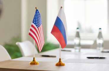 USA and Russia flags standing on table in meeting room with papers and bottles of water. Concept of international relations, diplomatic negotiations between global political or economic partners.