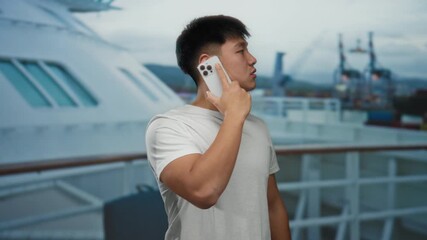 Young man talking on smartphone aboard cruise ship with sea view in background conveying leisure travel and connectivity outdoors.