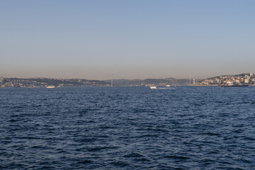 Obraz premium Scenic Bosphorus Strait in Istanbul at sunset with urban skyline, iconic bridges, fishing boats, and calm sea, highlighting the beauty and cultural heritage of Turkey’s most famous waterway