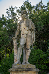 Fototapeta premium An old statue of Hercules with sunlight in the background and trees. 
