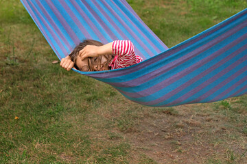 A cute funny girl with glasses is swinging on a striped hammock straightening curly disheveled hair