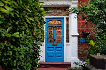 Blue victorian front door with stained glass windows is surrounded by green bushes