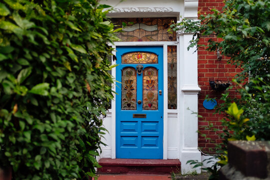Blue victorian front door with stained glass windows is surrounded by green bushes - Powered by Adobe