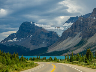 Fototapeta premium Car driving along Icefields Parkway toward towering Rocky Mountains