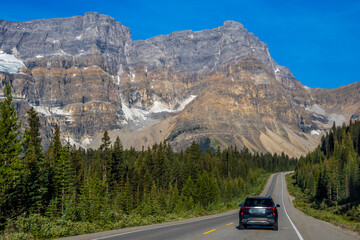 Car driving along Icefields Parkway toward towering Rocky Mountains