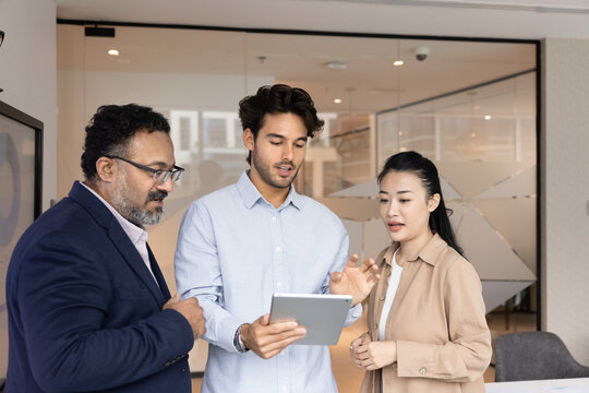 Digital data in business dialogue. Diverse multiracial businesspeople group stand in office use tablet pc to discuss online document create ideas for marketing plan develop product promotion strategy