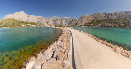 Stone breakwater leading into the sea with mountains in the background in Omis Croatia