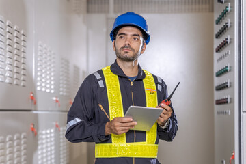 Confident engineer in blue jumpsuit holding laptop computer, walkie-talkie  in a warehouse. Shot of a engineer using a digital tablet on a construction site.Caucasian professional Engineer factory. 